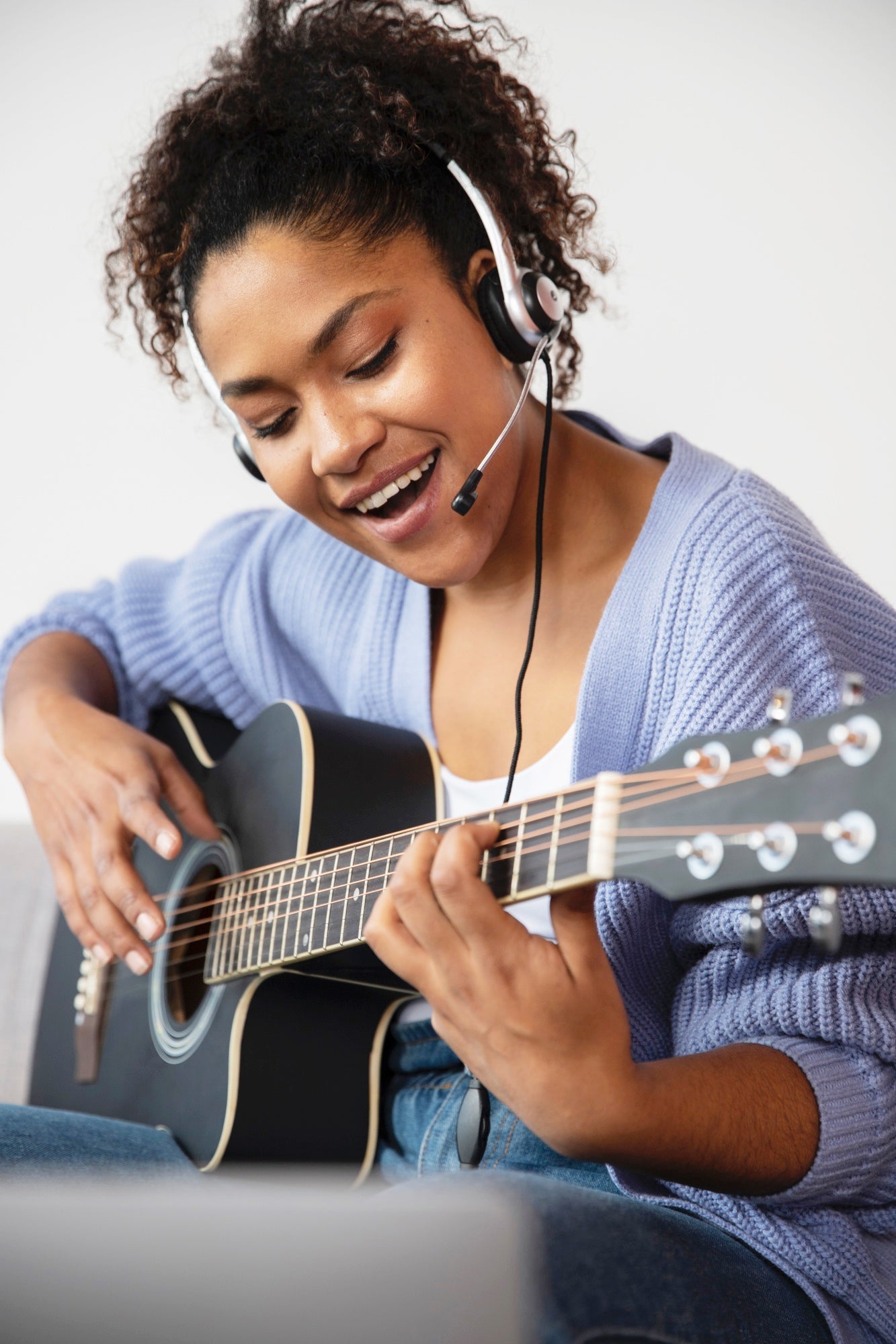 Eine Frau spielt Gitarre, hat ein Headset auf und singt.